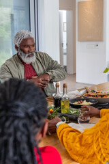 African American family sharing meal at home table with senior wearing green jacket near salad