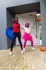Naklejka premium African American preteen and child girls posing at front door wearing capes, tutu, pumpkin, web