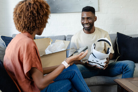 Couple unboxing white VR headset on sofa, open box with bubble wrap, holding headset, copy space