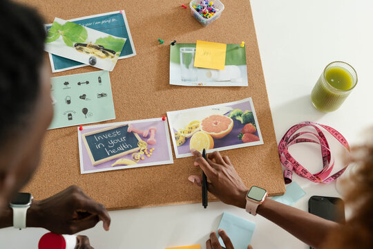 Cork board is showcasing pinned fruit photos and health card on white table, with green juice