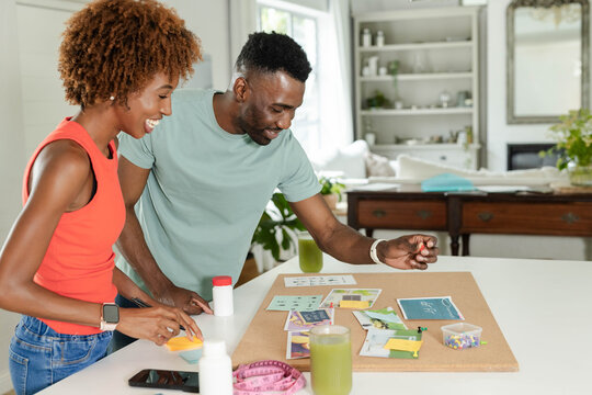 African American couple arranging corkboard display at home on white counter holding sticky notes