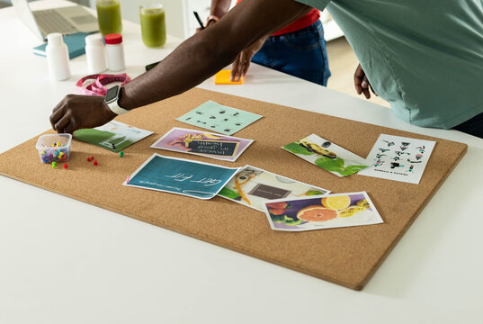 Cork bulletin board sitting flat on white table, covered with printed cards and scattered push pins