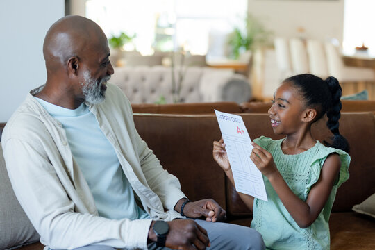 African American father and child celebrating on brown sofa, holding report card showing letter A+