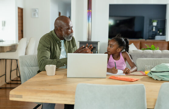 Senior African American man and Child African American girl teaching at table with laptop, notes