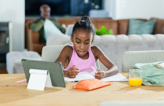African American family youth female studying at home table using tablet stand workbook pencil case