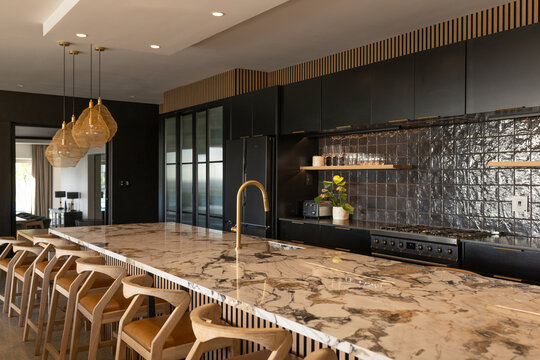 Marble island anchoring kitchen, featuring brass faucet, wooden stools and black cabinets