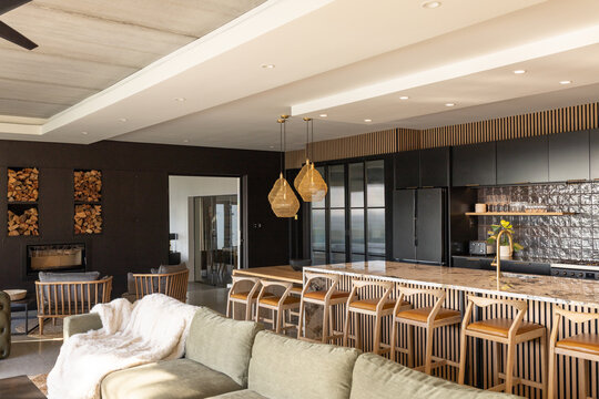 Kitchen island is anchoring open-plan interior, showing marble countertop, six wooden bar stools