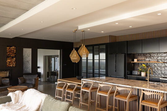 Marble island featuring wooden slats and holding six leather stools, woven pendants casting warmth