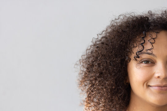 Woman smiling while posing in studio, showing curly hair stud earring, copy space