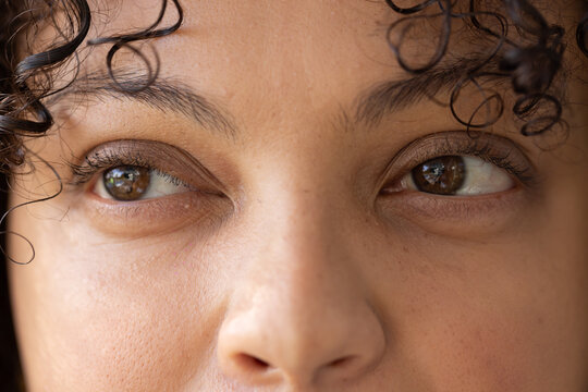 Woman focusing on eye area, gazing slightly right in room with window reflections and curls