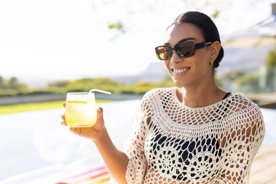 African American woman by pool, smiling in crochet coverup holding glass and straw, copy space