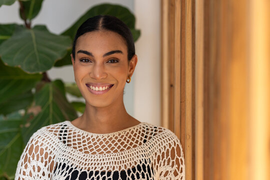 African American woman smiling, wearing crochet top over dark camisole in studio with fig plant