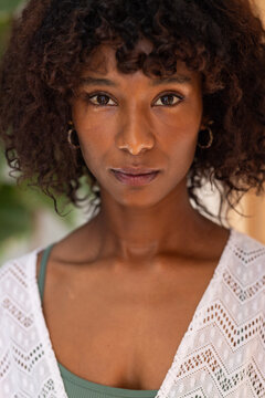 African American woman posing in studio with foliage, warm wall, white lace top, green tank, hoops