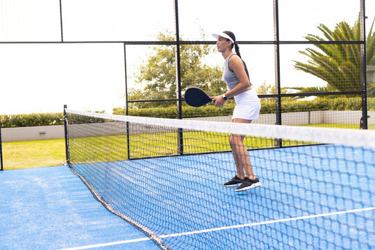 African American woman in white visor playing on court at net holding black paddle, copy space