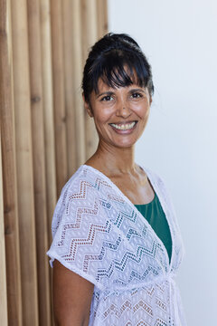 Mature African American woman posing, smiling in studio by wood panel, wearing white knit cover-up