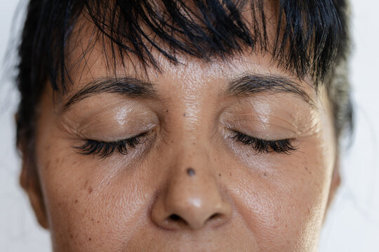 African American mature woman filling frame, closing eyelids, revealing eyelashes, mole in studio