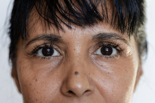 Mature African woman filling frame, highlighting eyes, eyelashes, nose mole and skin texture studio