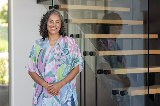 African American woman posing by floating stairs with glass panels in entry, wearing pastel kaftan