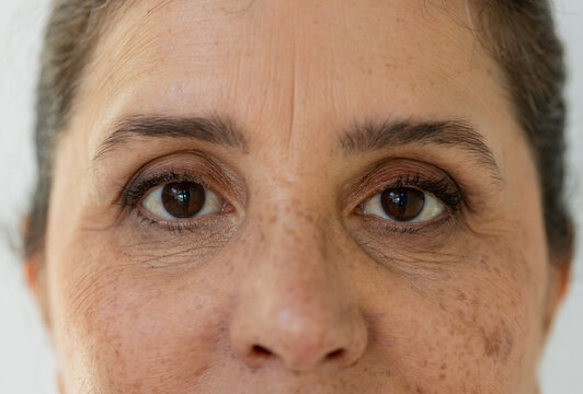 Mature woman looking directly at camera in studio, showing freckles, mascara, skin texture
