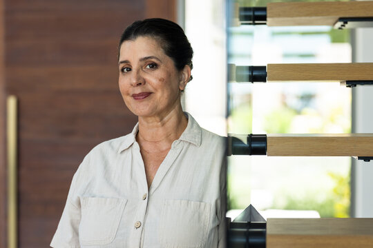Mature woman wearing beige shirt standing in entry near open-riser staircase with brass handle