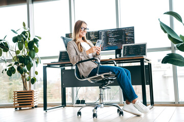 Smiling female programmer working remotely in a modern office with multiple monitors and...