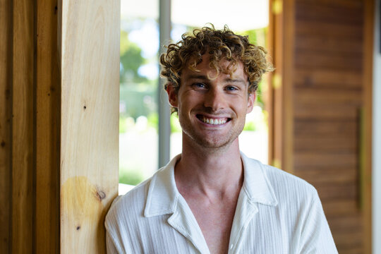 Adult man leaning on wooden post, smiling, wearing textured shirt by glass window and slatted wall