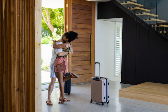 Couple hugging, reuniting at modern entryway, holding crossbody bag and two rolling suitcases