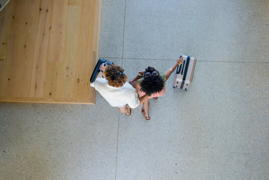 Couple walking across concourse by wooden bench pulling two suitcases with sunglasses and sandals