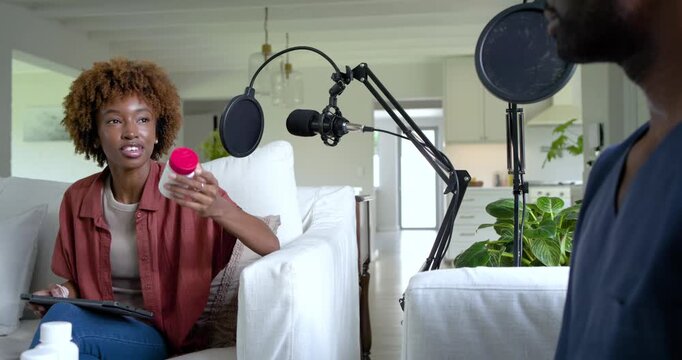 Podcast hosts at home, African American woman reaching for bottle near mic while man examining it