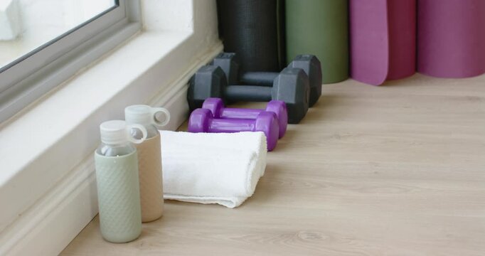 Camera is starting to record and holding steady on bottles towel dumbbells near window for workout