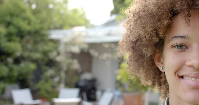 Woman is stepping into frame from right on backyard patio, smiling and laughing near grill