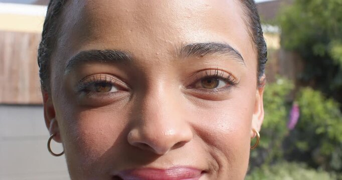 Adult African American woman smiling, blinking, reacting to sun in garden, showing gold hoops