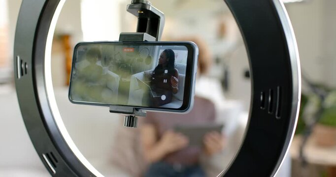 African American woman tapping tablet shifting on sofa after smartphone pause in ring light clamp