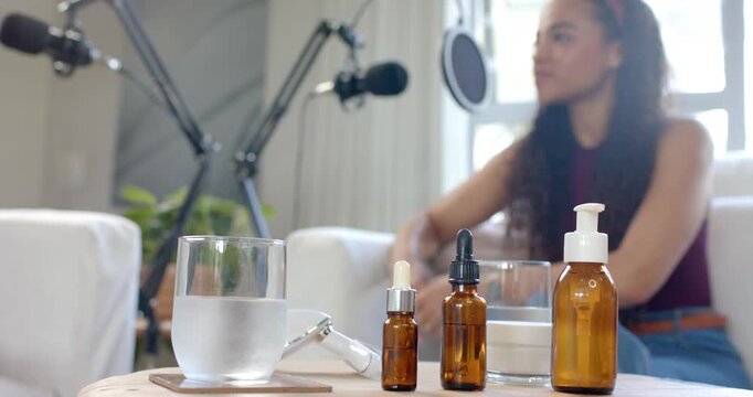 African American woman on sofa talking into mic, answering host cues for podcast, amber bottles
