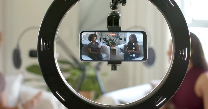 African American women sitting in home studio, ring light flashing, smartphone recording interview