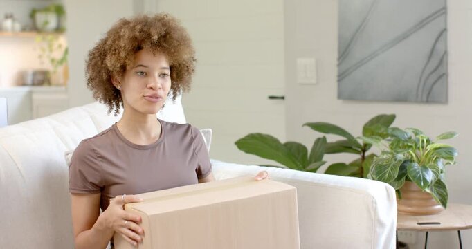 African American woman and pal speaking holding opening box on sofa tilting toward tablet to show