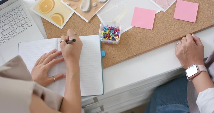 Right designer is reaching for pin, is arranging pictures on moodboard while left is writing notes