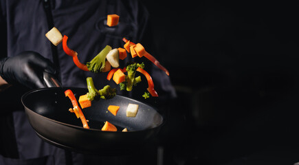 Chef tossing vegetables in pan with black background