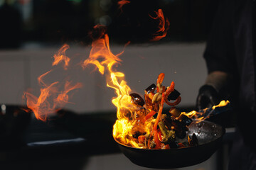 Dramatic stir fry flames in kitchen with vegetables on fire, man chef prepares food © Parilov