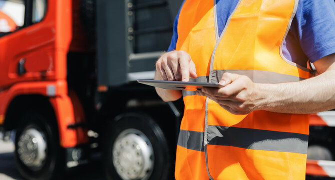 Concept banner automated logistics online internet. Dump truck driver man in uniform with tablet computer controls loading of cargo