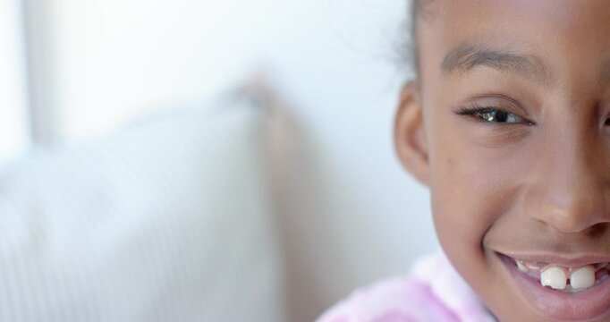 African American child smiling and blinking reacting to offscreen cue on sofa by window, copy space