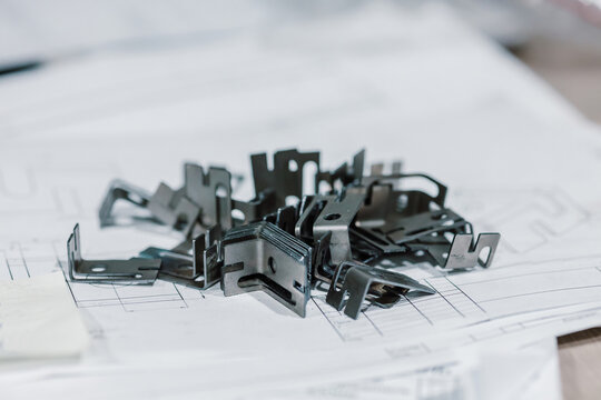 Small metal brackets and steel parts lying on engineering blueprints in a design office.