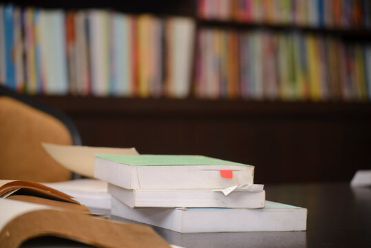 Desk for student education concept. Stack of Books for study for exam placed on wooden School table with library shelf wall background for student plan to work.