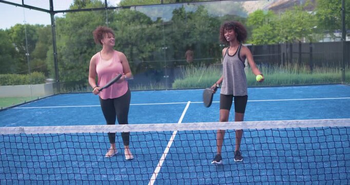 African American women after chat in tanks holding paddles practicing forehand swings on blue court