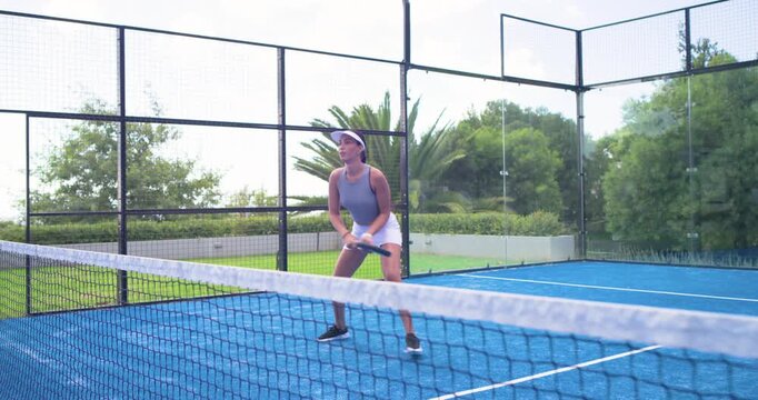 Two African American women, front player volleying on incoming shot on padel court holding paddle