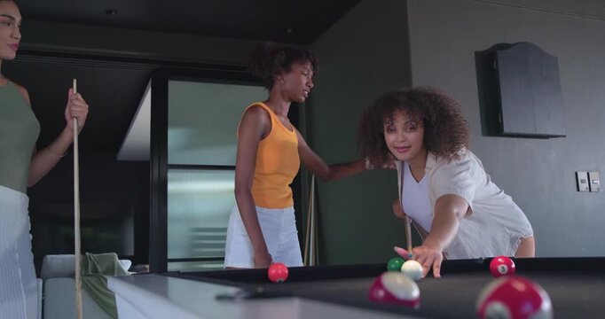 African American women after pointing, aiming, striking cue ball on pool table in lounge for fun