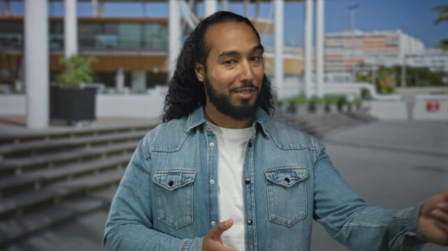 Man smiling and gesturing with hands in front of building steps at outdoor plaza; friendly conversation.