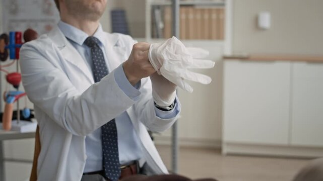 Broll closeup of male doctor wearing disposable gloves prior to medical checkup during urology appointment in contemporary clinical office with clean interior