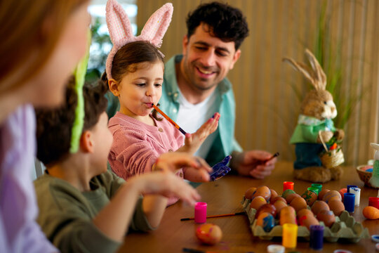 Little girl painting easter eggs with family at table