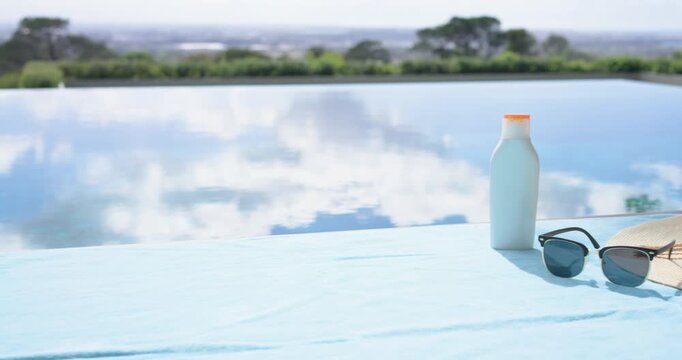 Blue bottle entering right while sunglasses and straw-hat are forming still-life on cloth by pool
